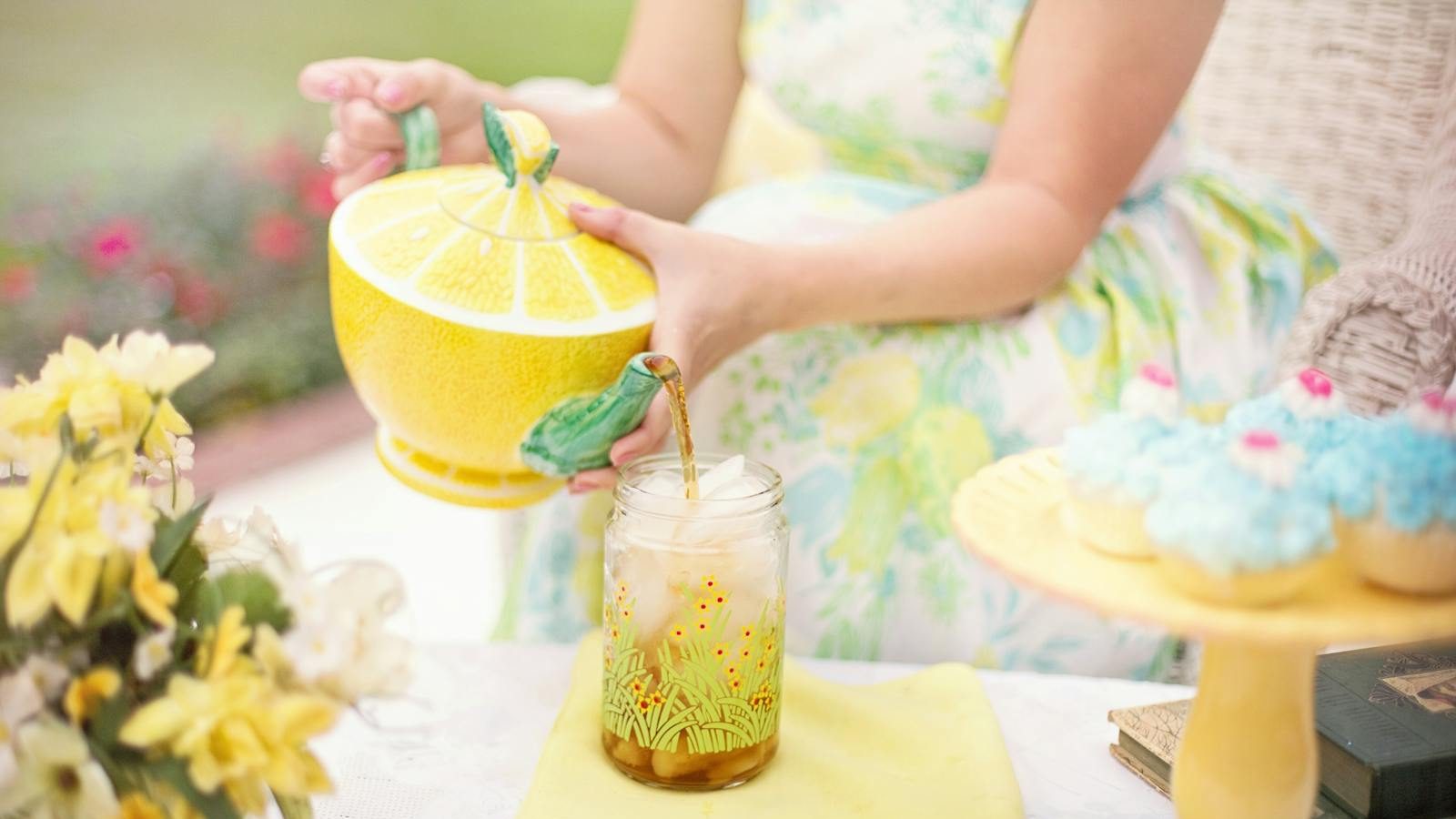 Enjoy a delightful outdoor tea party with iced tea, cupcakes, and floral decor in a serene setting.