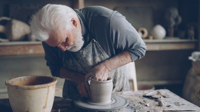 An older man is shaping clay on a wheel.