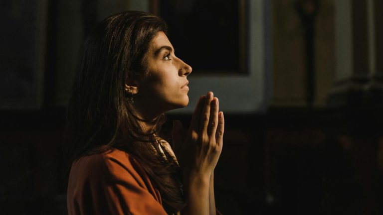 Side profile of a woman praying indoors with hands together, creating a serene and religious ambiance.