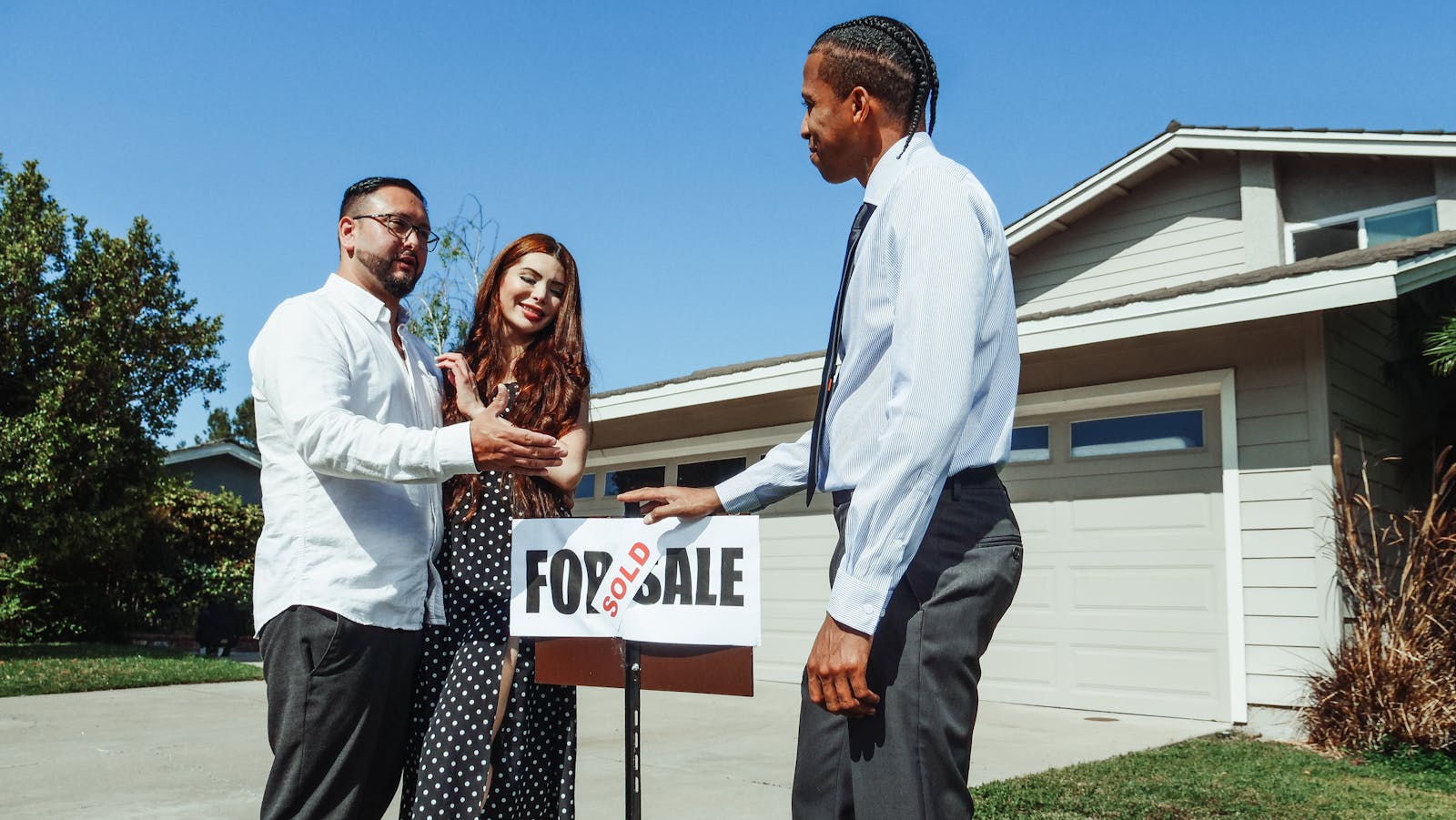 A couple meets with a realtor to finalize the purchase of their new home, indicated by a 'Sold' sign.