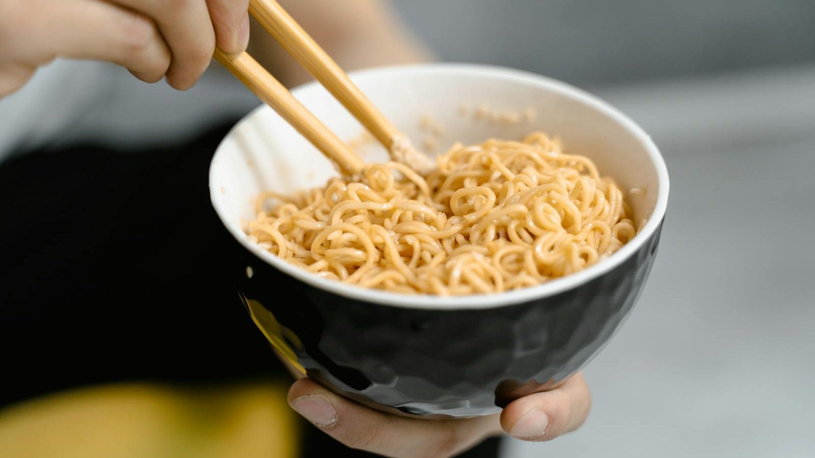A person holding a bowl of noodles with chopsticks, captured in a close-up shot.