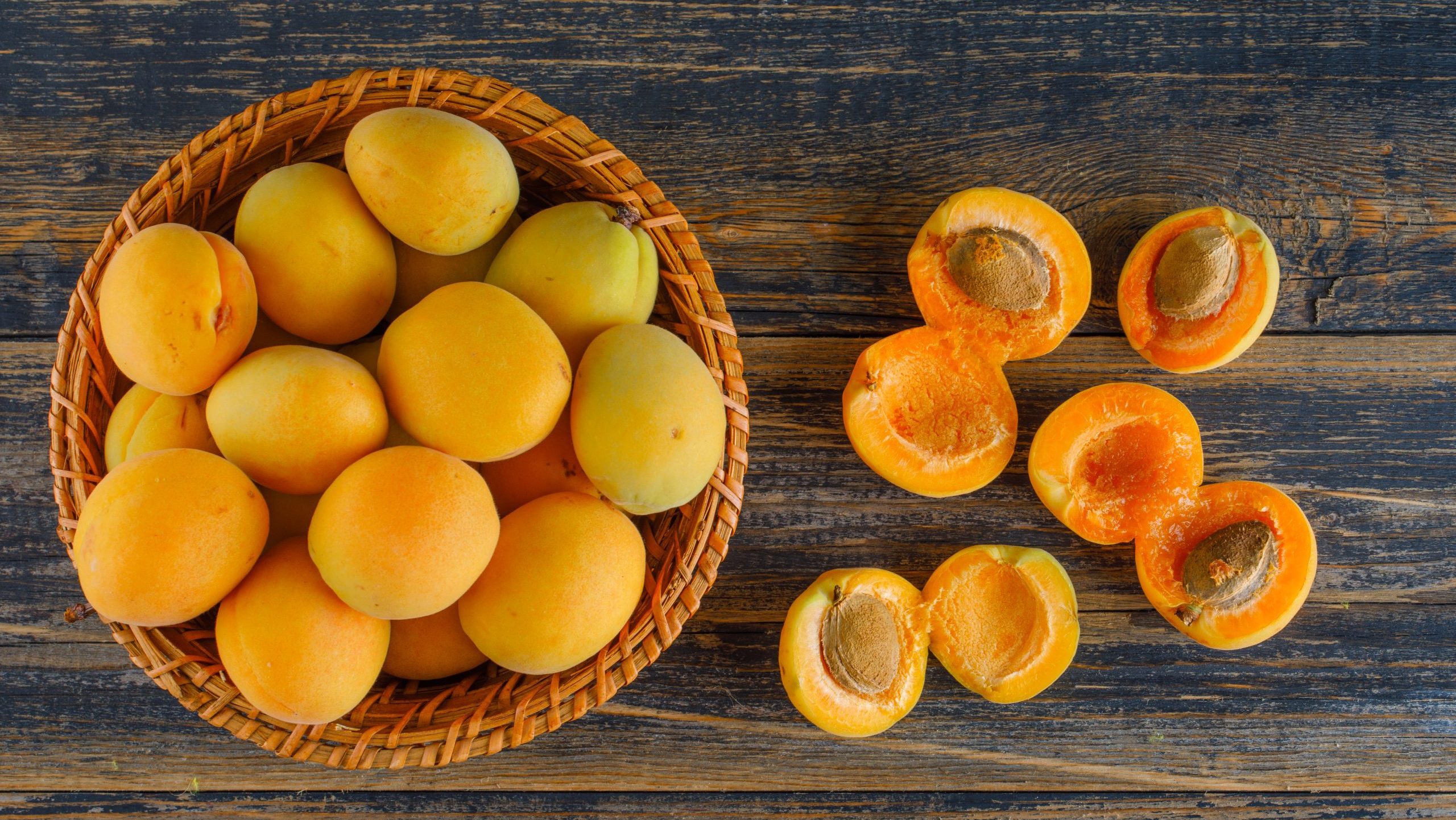 Apricots in a wicker basket on wooden background, flat lay.