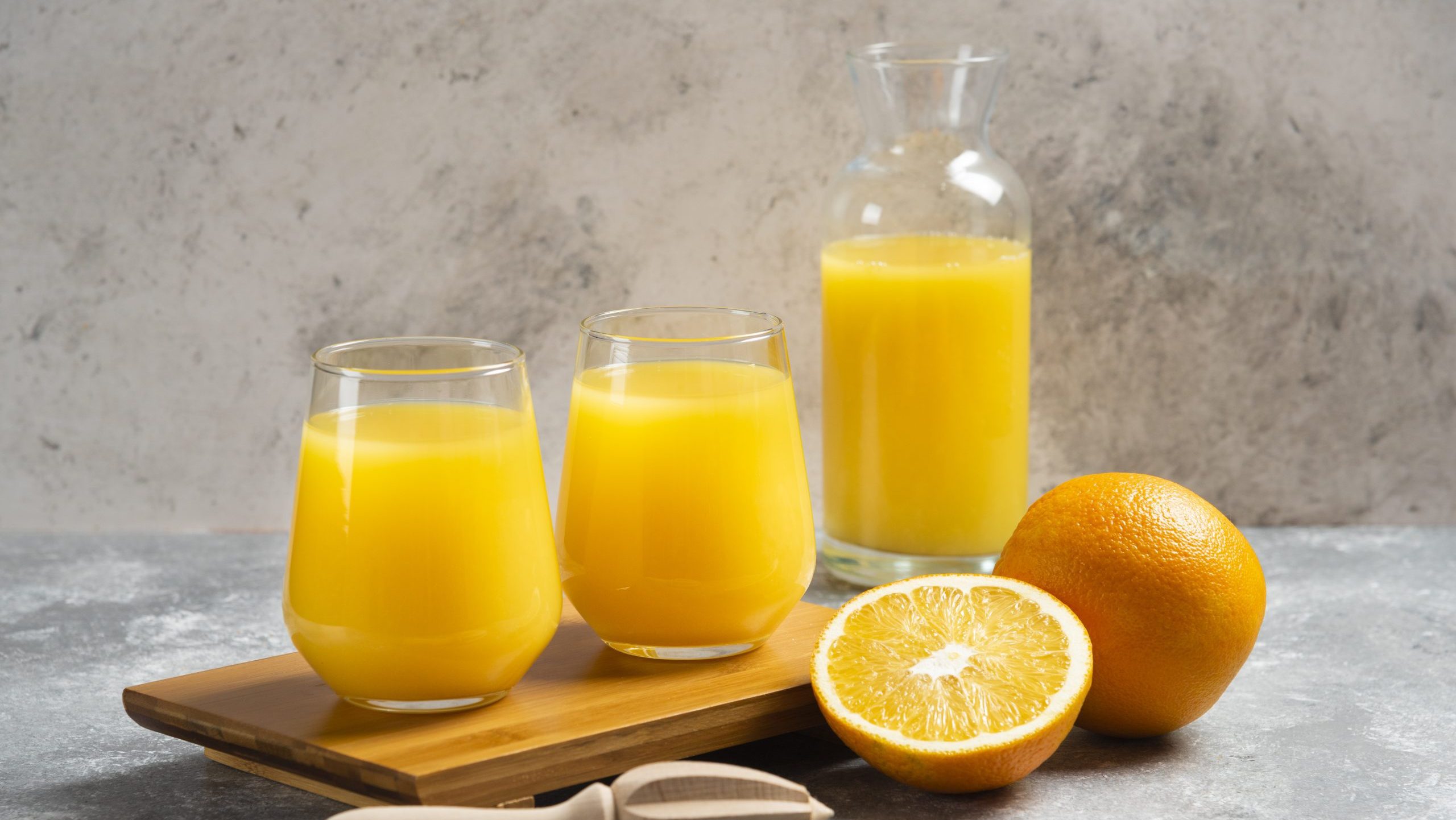 Glass cups of orange juice and a wooden reamer