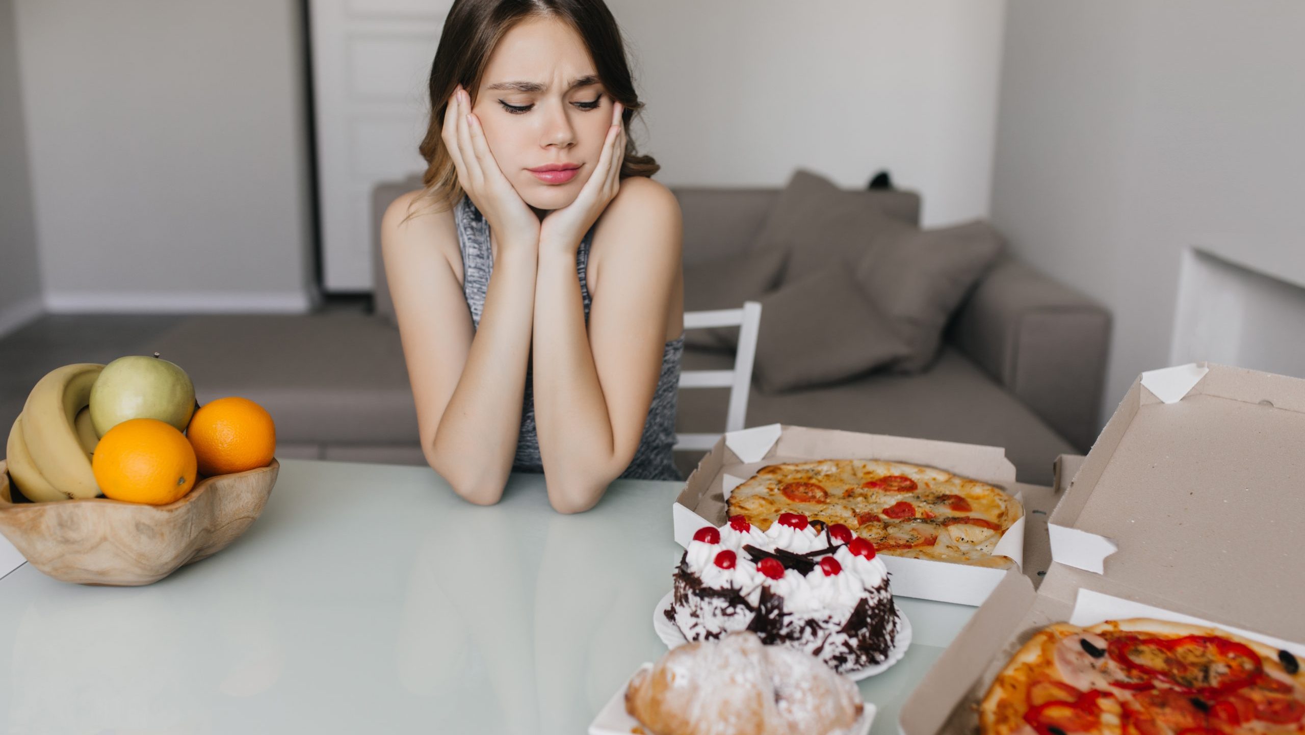 no-snacking-after-dinnerSad curly woman looking at cake during diet. Blonde gorgeous female model posing with fruits and pizza.