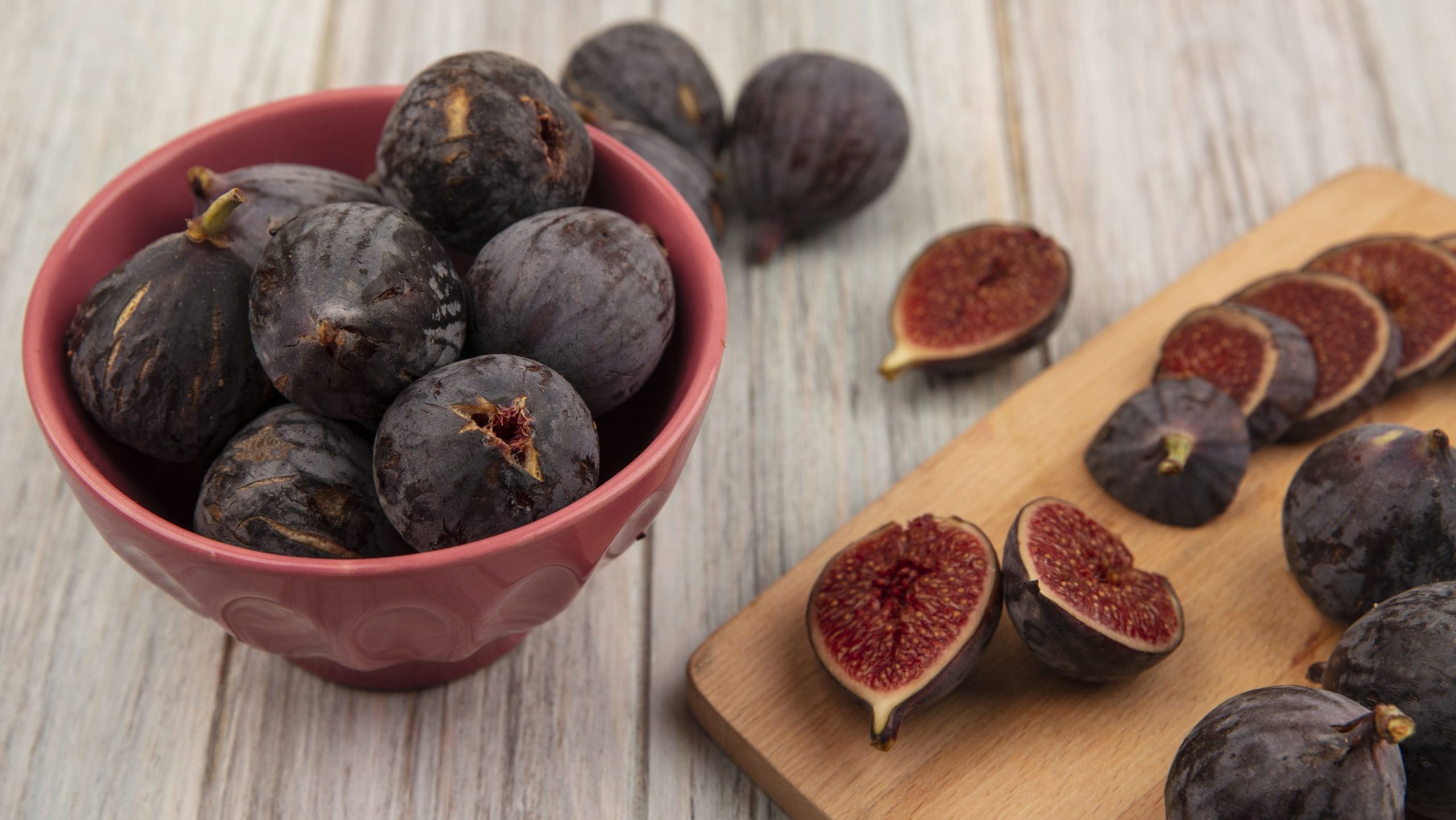 top view of delicious ripe black mission figs on a wooden kitchen board with black figs on a bowl on a grey wooden background