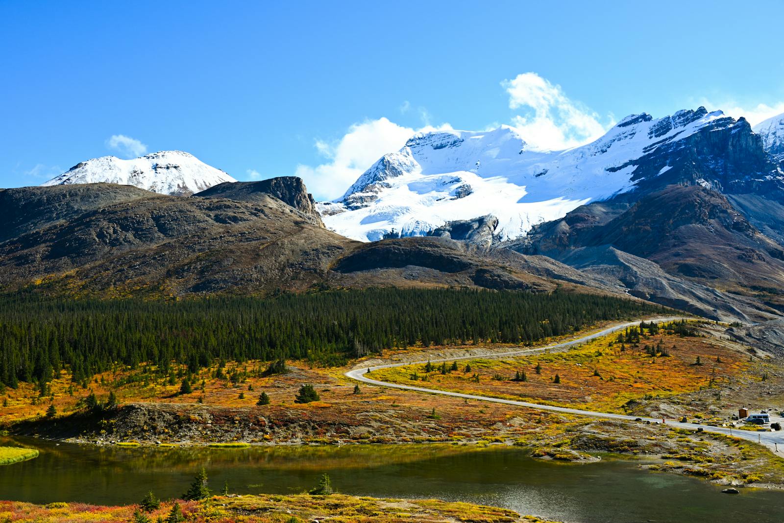 Breathtaking autumn view of Jasper National Park with snow-capped mountains, vibrant foliage, and a winding river.
