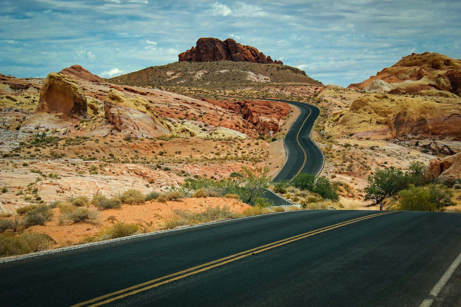 Scenic desert highway curving through vibrant sandstone hills under a cloudy sky.