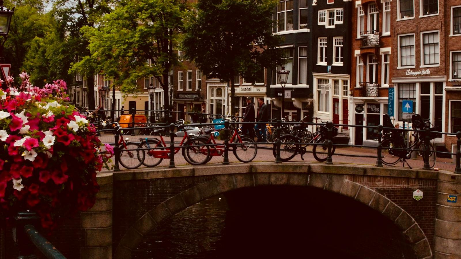 Scenic view of an Amsterdam canal bridge adorned with bicycles and vibrant flowers, perfect for urban travel inspiration.