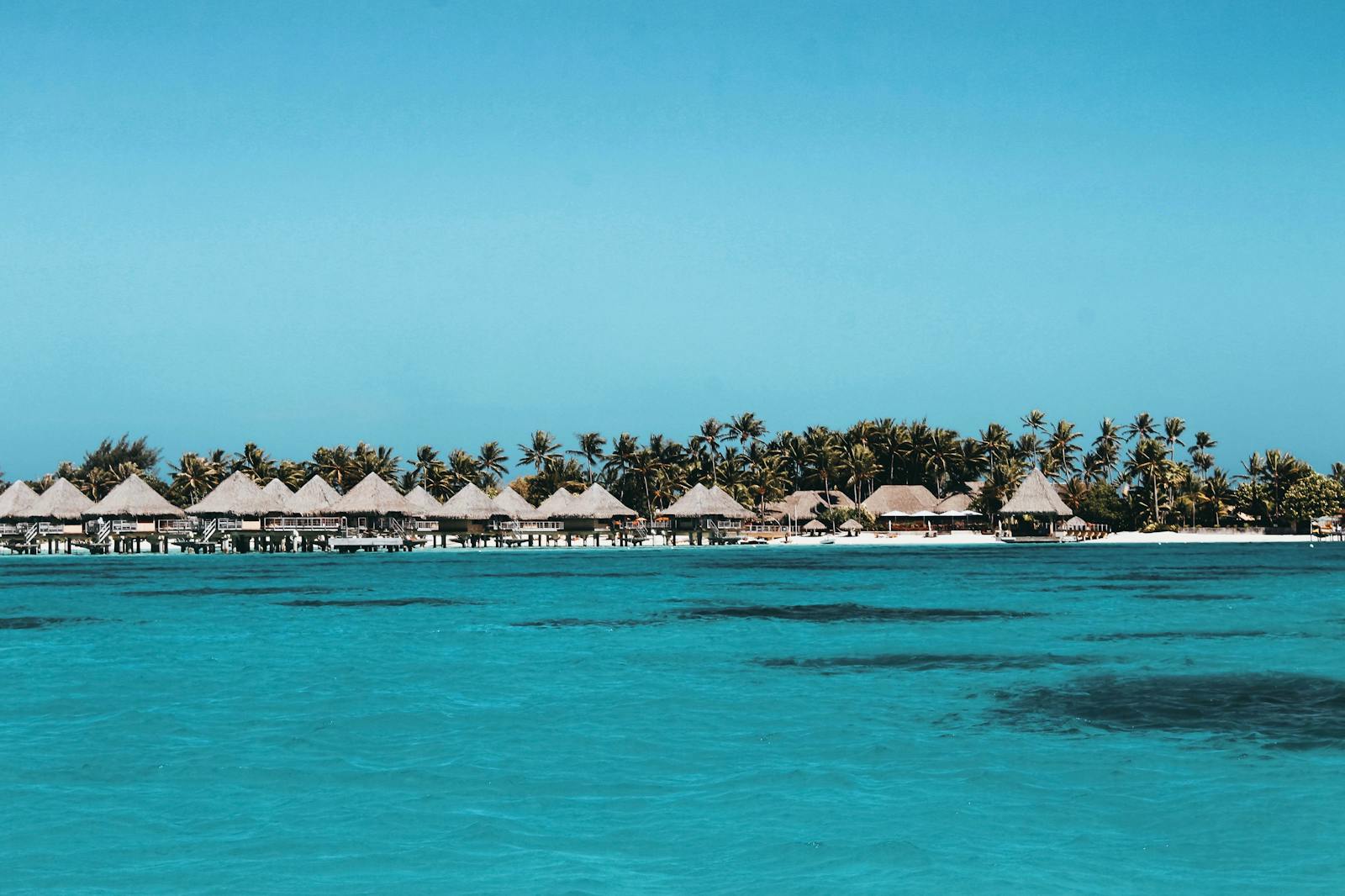 Idyllic bungalows line the turquoise waters of Vaitāpē, French Polynesia, showcasing a serene tropical paradise.