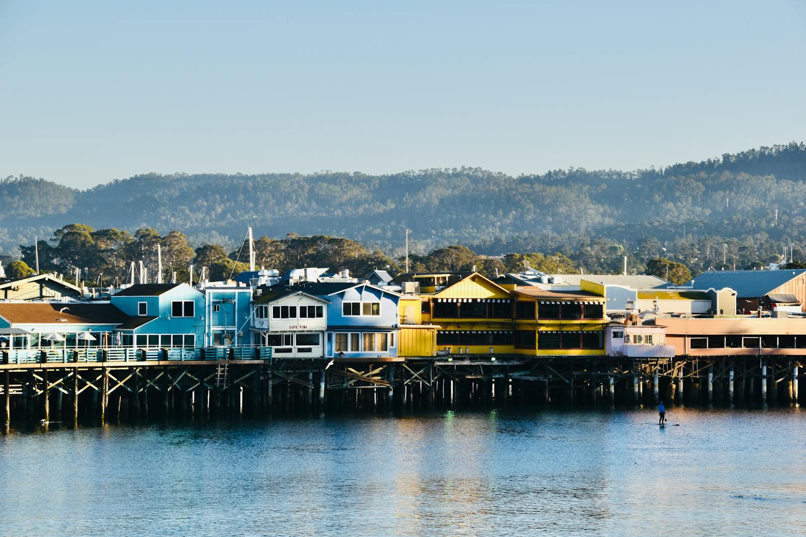 Colorful buildings at Old Fisherman's Wharf in Monterey, CA, reflecting on a calm bay under clear skies.
