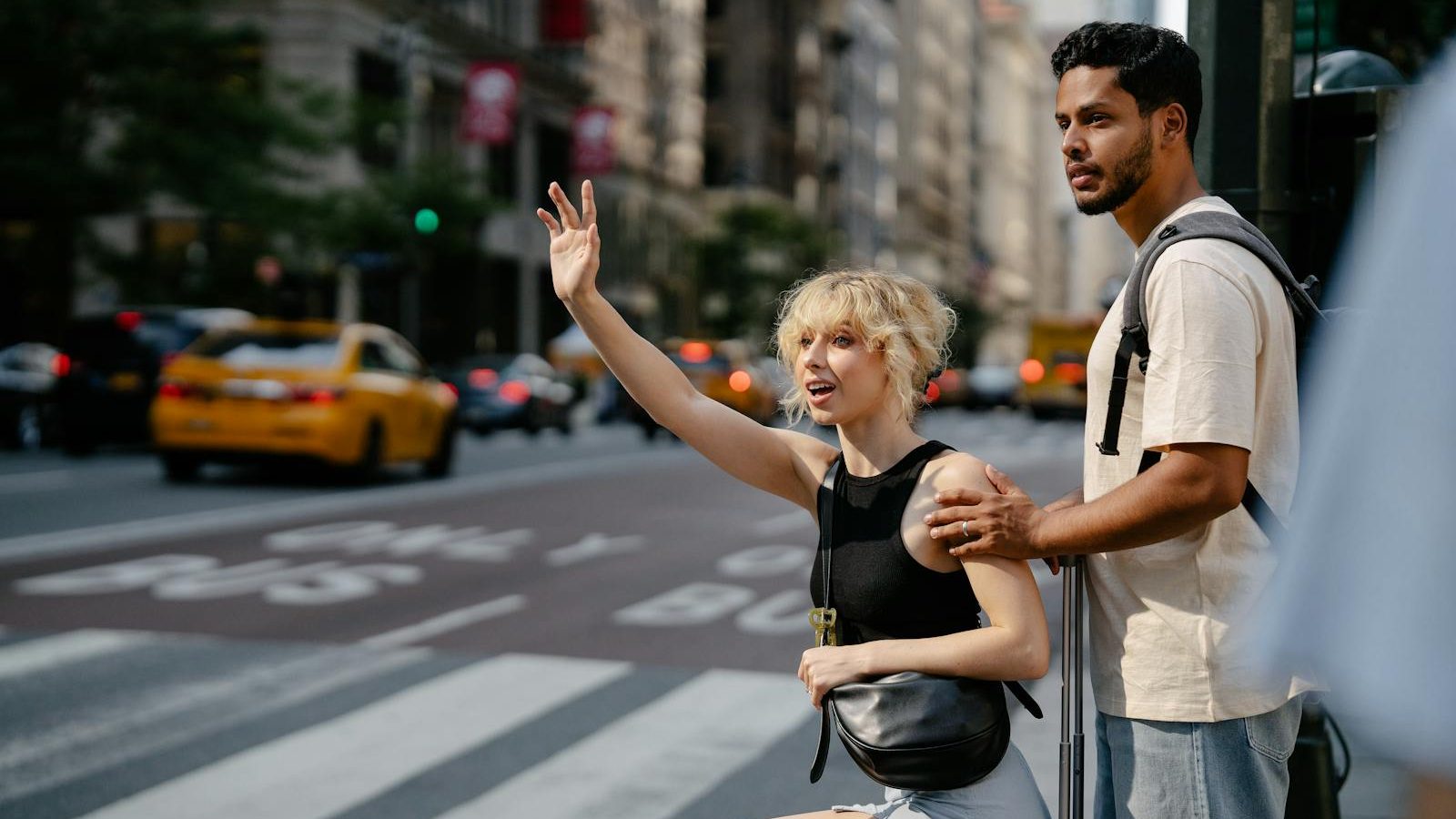 A young couple hailing a yellow cab on a bustling city street, exuding urban life.