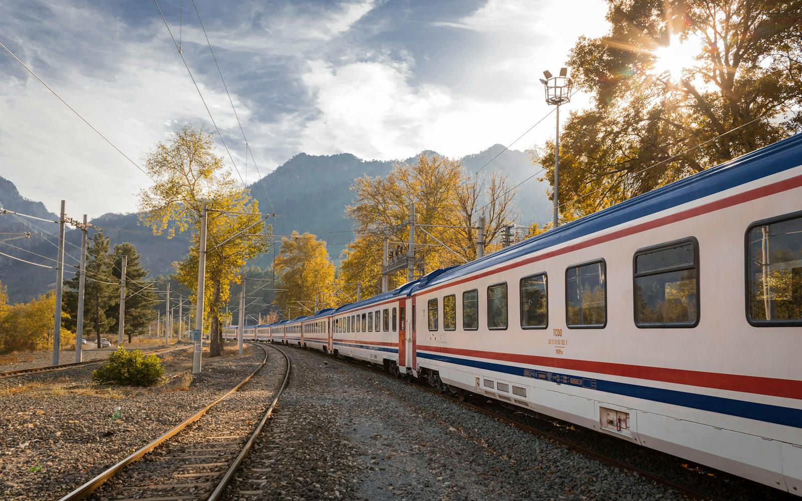 A picturesque train travels through a vibrant autumn landscape with mountains.