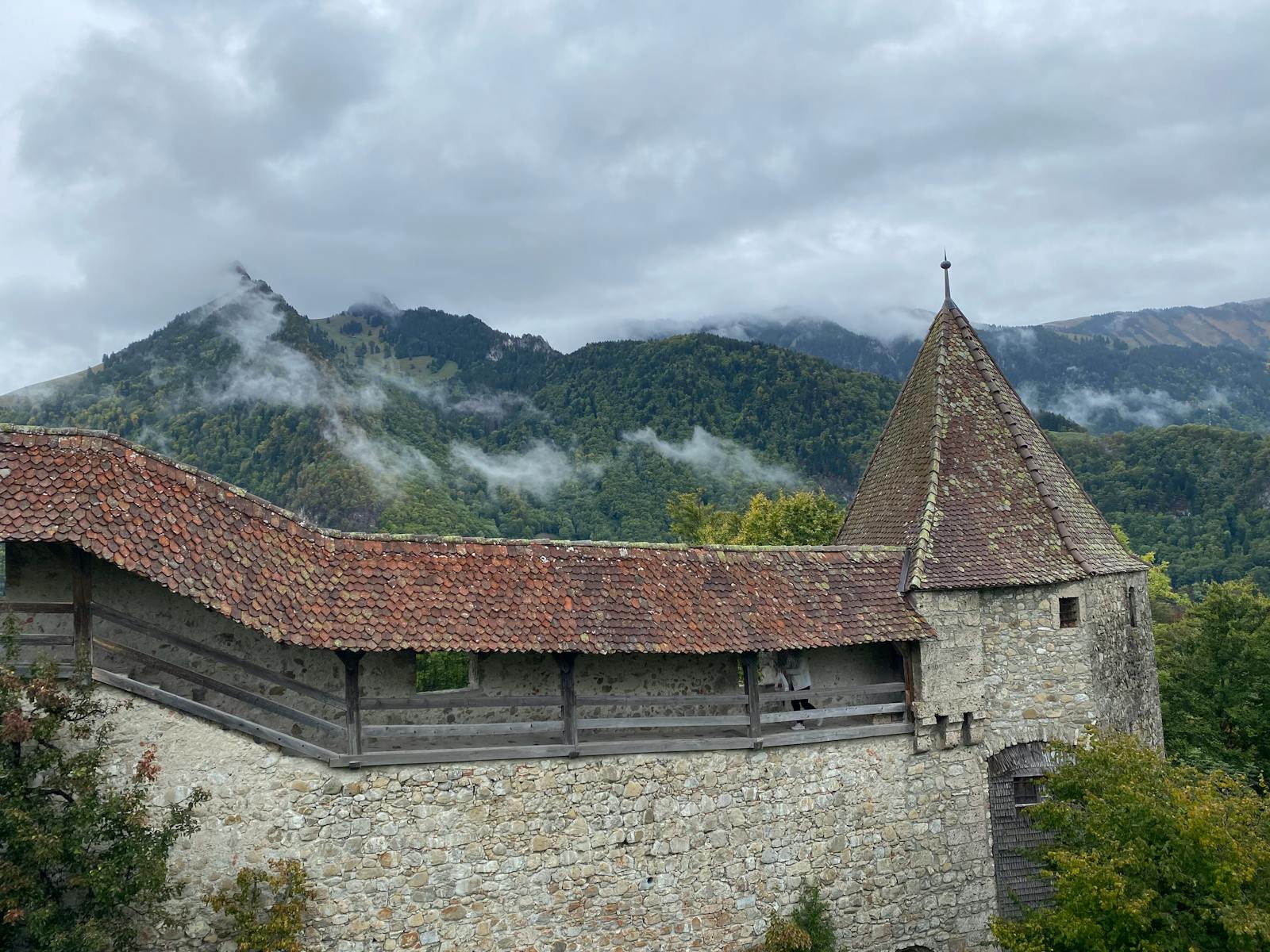 Scenic view of medieval stone architecture in Gruyères, surrounded by misty mountains.