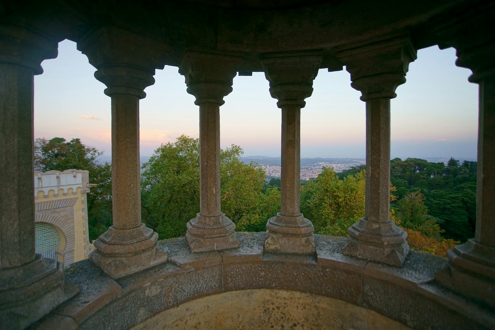 Gothic-style columns frame a scenic view of Sintra's lush landscape and the distant city.