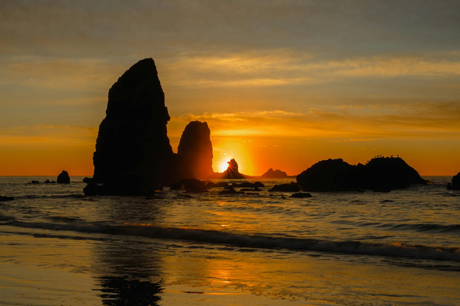 Stunning sunset over rock formations at Cannon Beach, Oregon, capturing the warm, vibrant sky and serene shore.