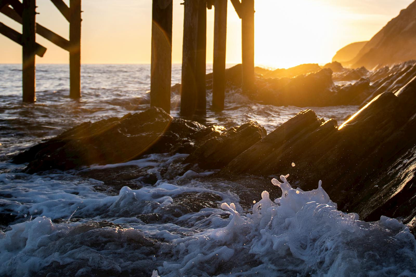 Capture the tranquil beauty of a sunrise at Gaviota Pier with waves crashing on rocky shore.