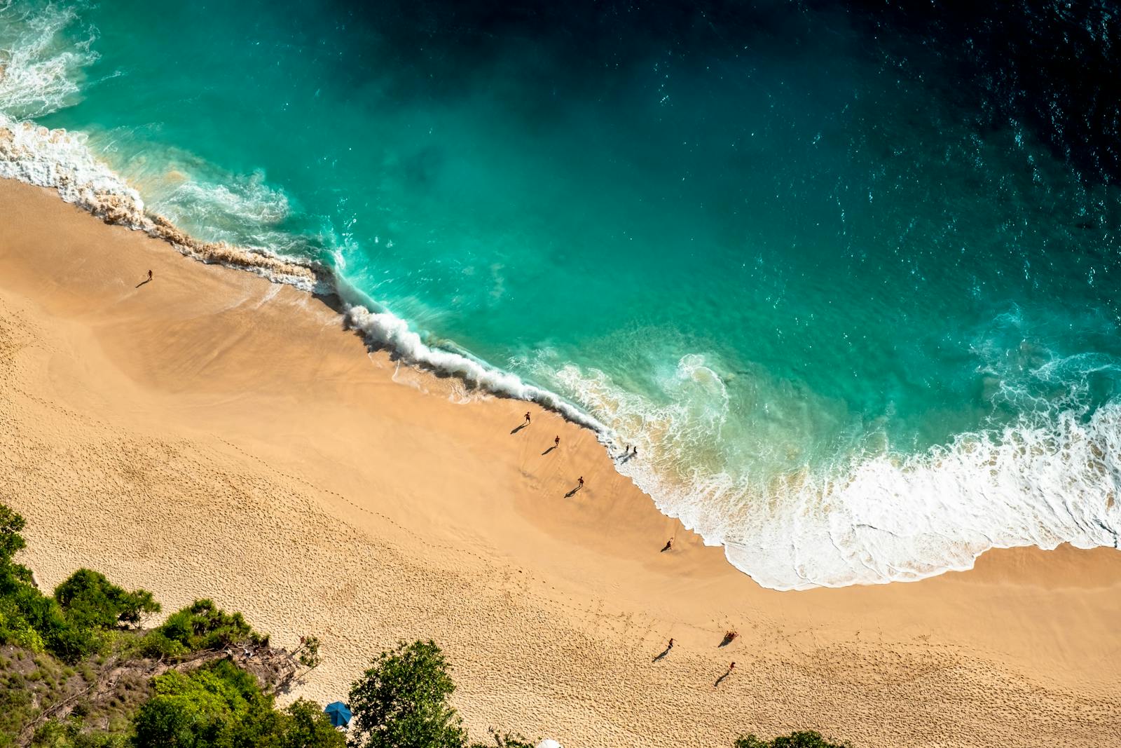 Stunning aerial view of Bali's beach with turquoise waves crashing on golden sand.