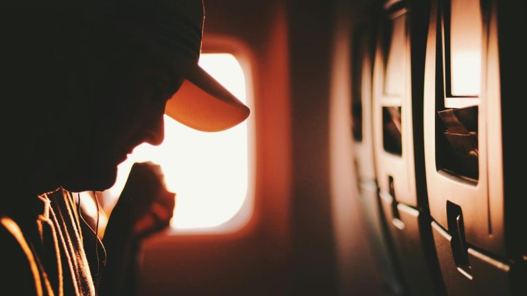 A silhouette of a traveler enjoying a quiet moment on an airplane, illuminated by sunrise through the window.