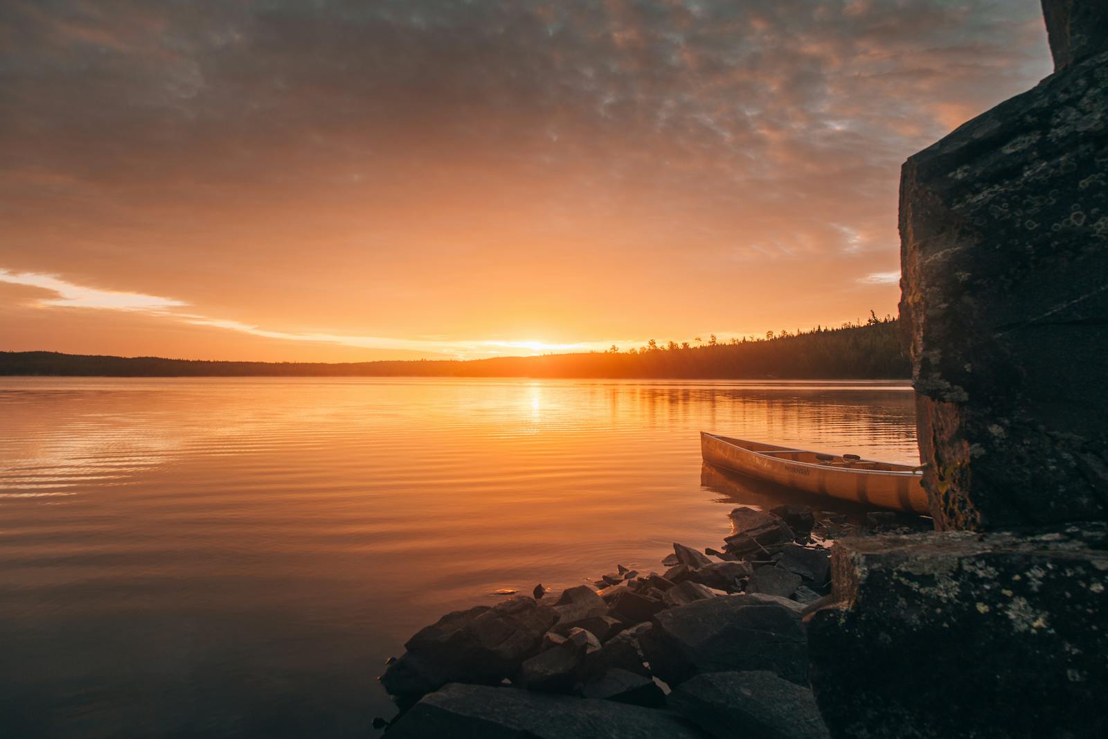 A tranquil sunset over a lake in Ely, Minnesota, featuring a canoe by the rocky shore.