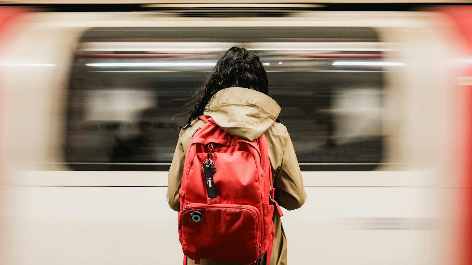 A person with a red backpack waiting as a train speeds past in the London Underground.