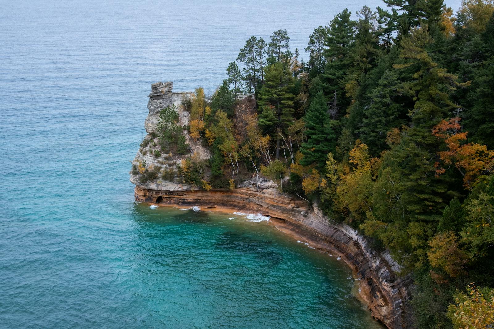 A stunning autumn view of Pictured Rocks in Munising, Michigan, with vibrant foliage and turquoise waters.