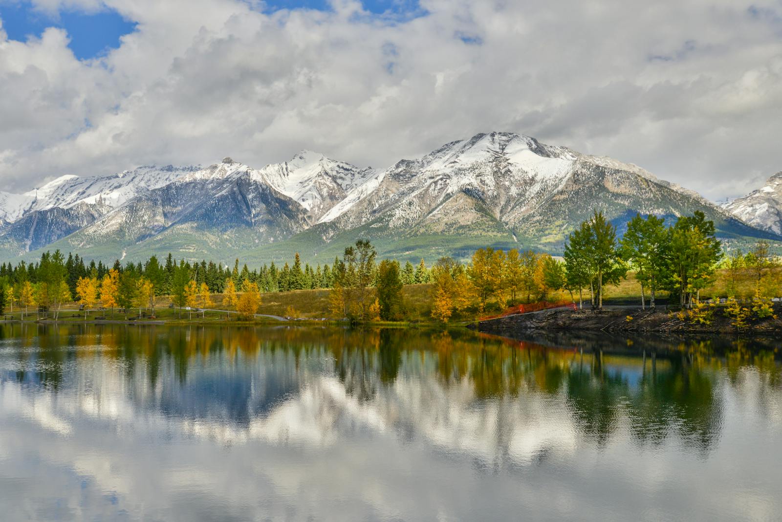 A serene autumn view of Canmore's snowy mountains reflecting in a calm lake.