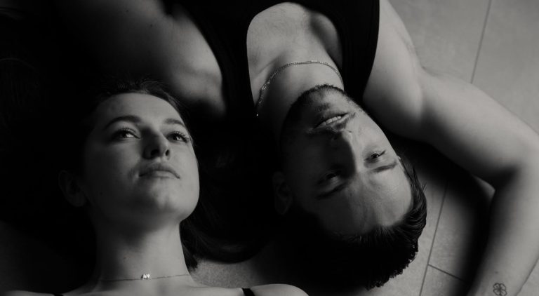Intimate black and white portrait of a couple lying on the floor, expressing tenderness and serenity.