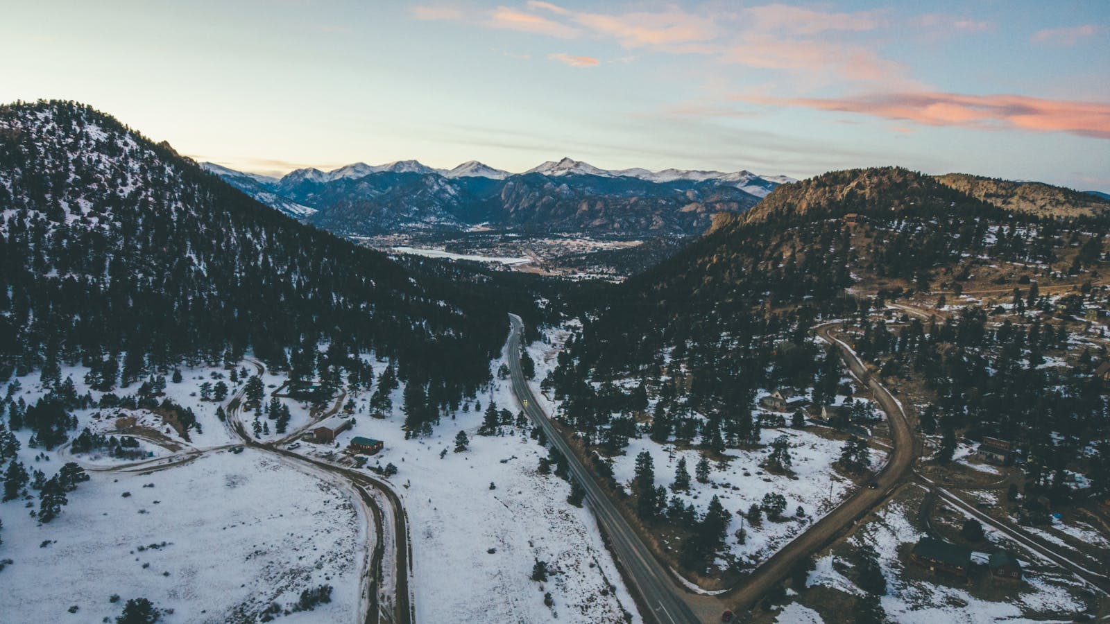 Drone capture of a winding road through snowy mountains during winter with scenic views.