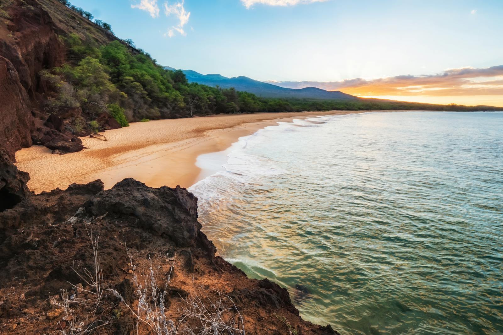 Breathtaking sunset view of Makena Beach, Maui with gentle waves and lush greenery.