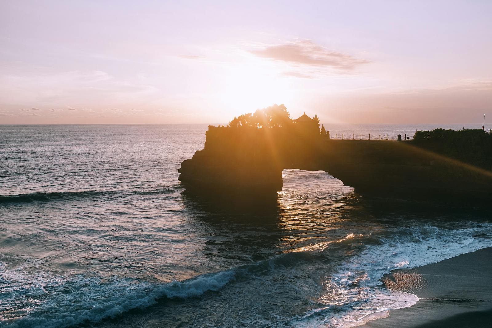 A breathtaking sunset view over the sea at Tanah Lot temple on Bali's rocky coast, offering serene beauty.