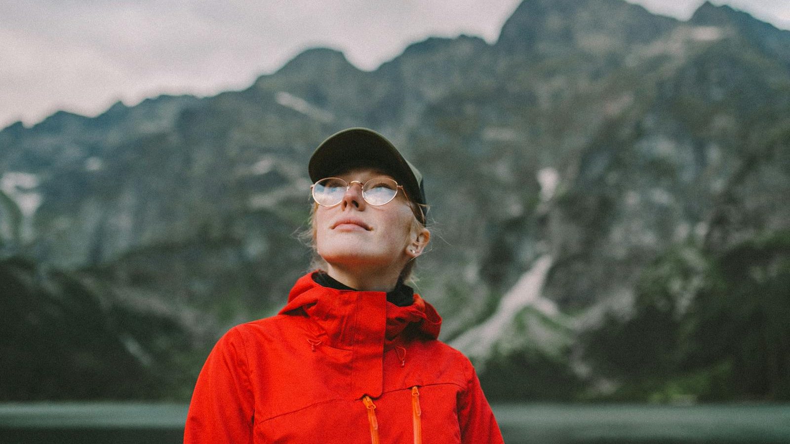 A young woman in a red jacket enjoying a serene mountain view, capturing the essence of adventure.