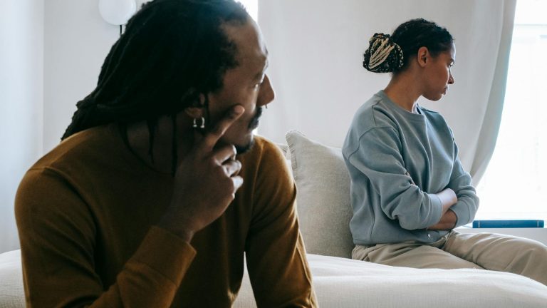 Young African American couple sitting on bed with sad face in casual outfit and thinking at home