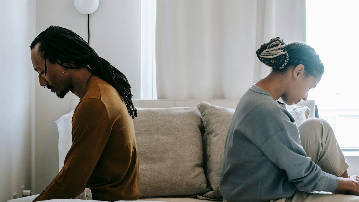 Side view unhappy sorrowful African American couple sitting on bed back to back after having argument