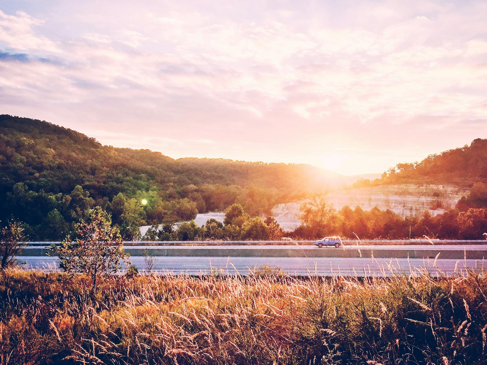 A serene highway scene at sunrise, with trees and hills creating a picturesque backdrop.