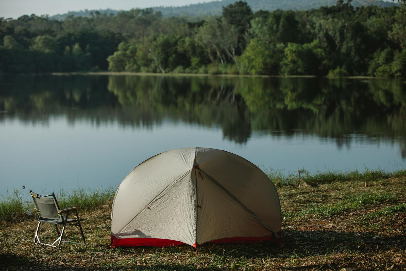 Idyllic lakeside campsite with tent and chair, reflecting nature's tranquility and summer serenity.