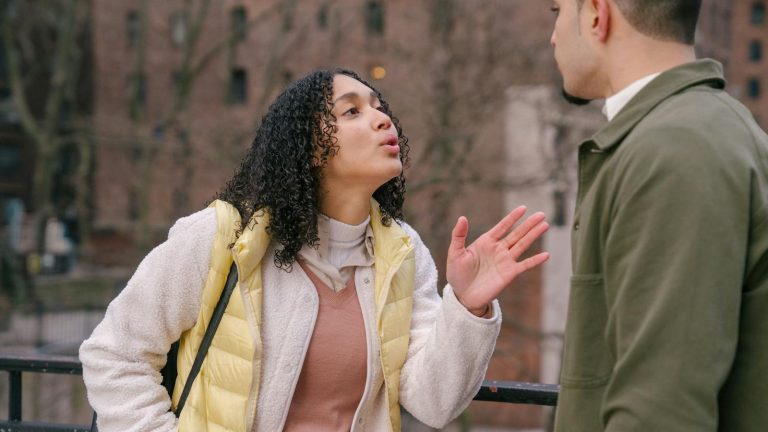 Young stylish Hispanic lady quarreling with crop boyfriend while standing together on city street