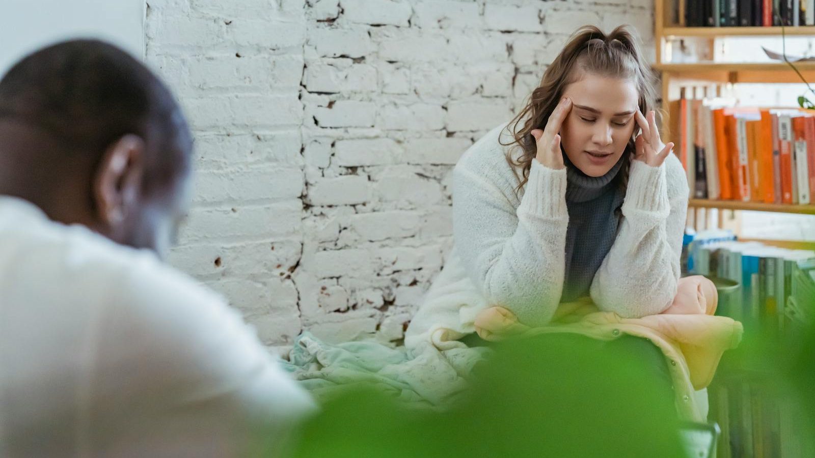 Exhausted woman calming down after argument with husband by putting fingers on temples and man sitting and looking down