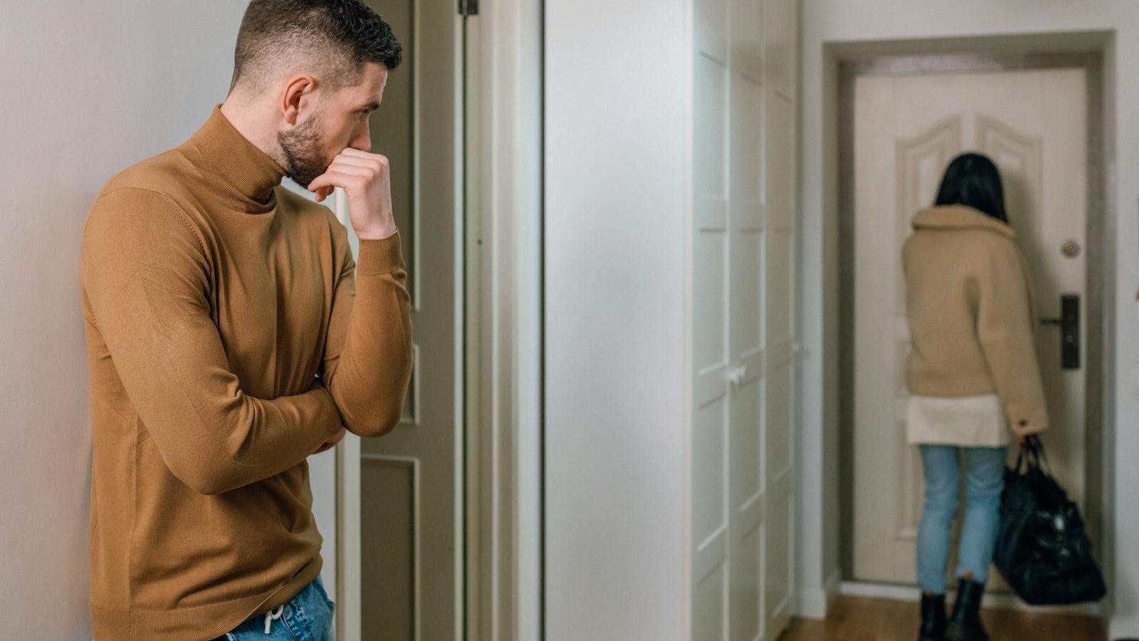 A couple experiencing a tense moment as a woman walks out of the apartment.