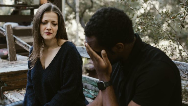 A couple experiencing emotional tension during a conversation outside on a bench.