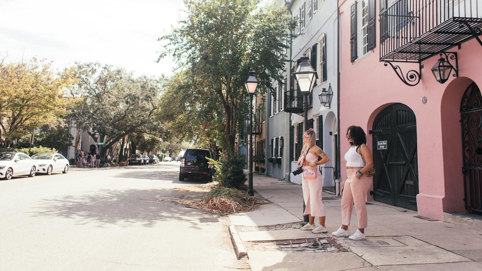 Two women stand on a vibrant urban street lined with pastel-colored buildings and trees.