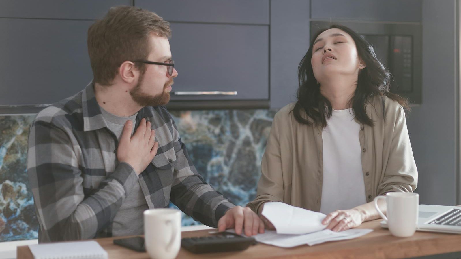 A couple experiencing stress while discussing finances in a modern kitchen setting.