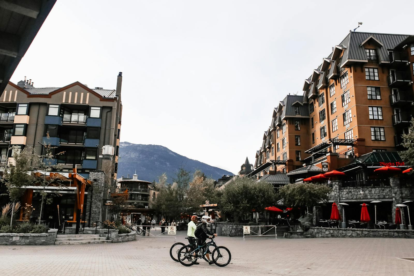 Cyclists riding through Whistler village surrounded by buildings and mountain scenery.
