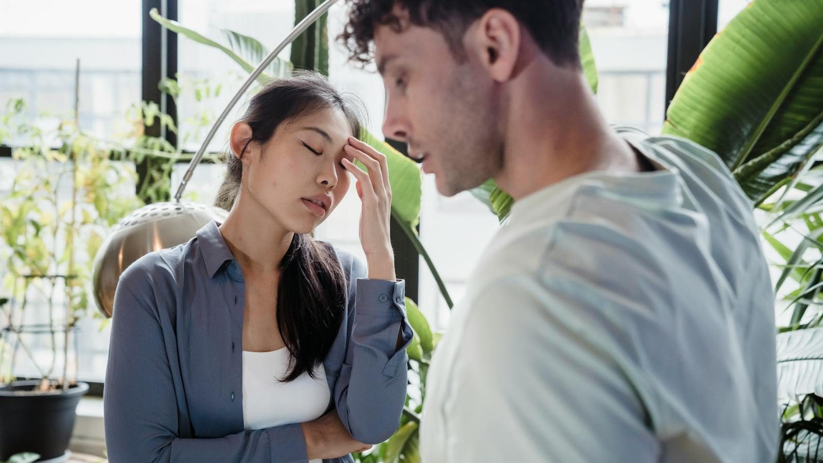 A couple experiencing a tense moment surrounded by plants in a modern space.