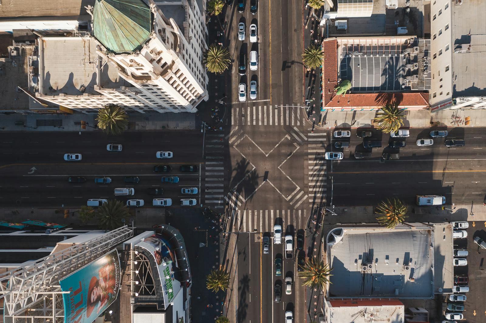 Aerial shot of a busy urban city intersection with cars and palm trees in daylight.