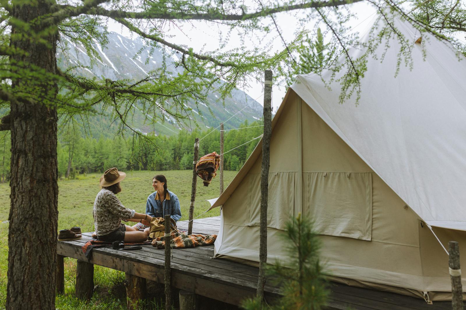 Couple enjoying a serene camping experience in a lush mountain forest beside a canvas tent.