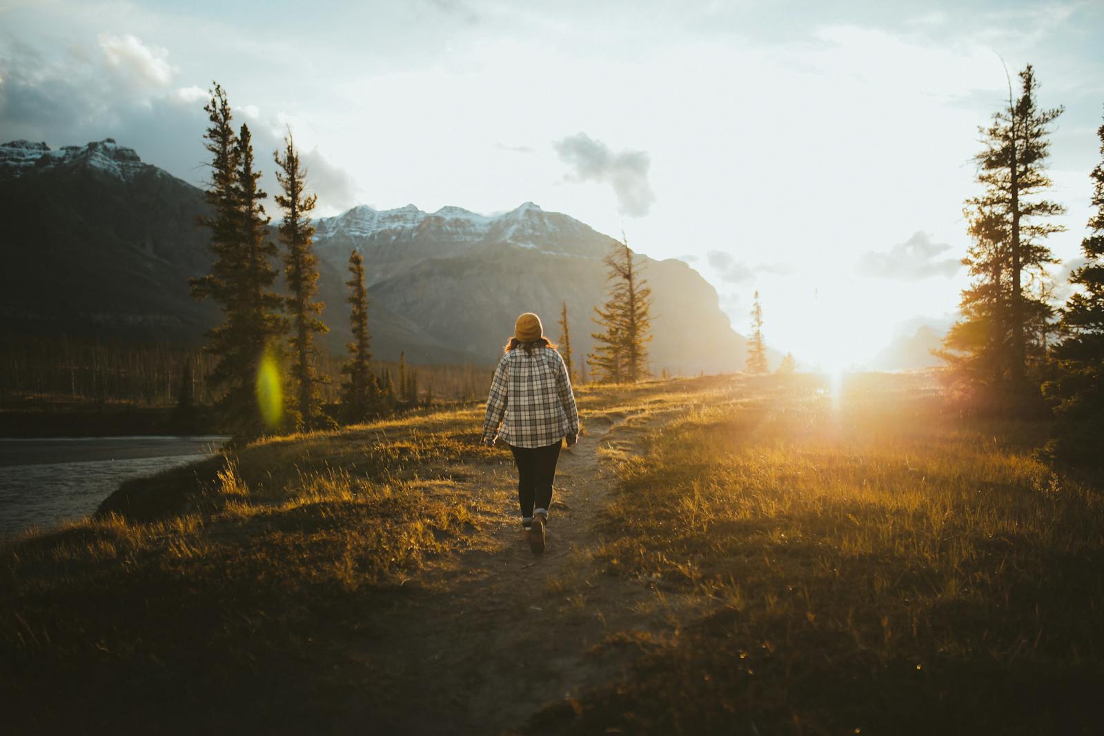 A person walks along a scenic trail in Alberta, Canada, with mountains in the sunset background.