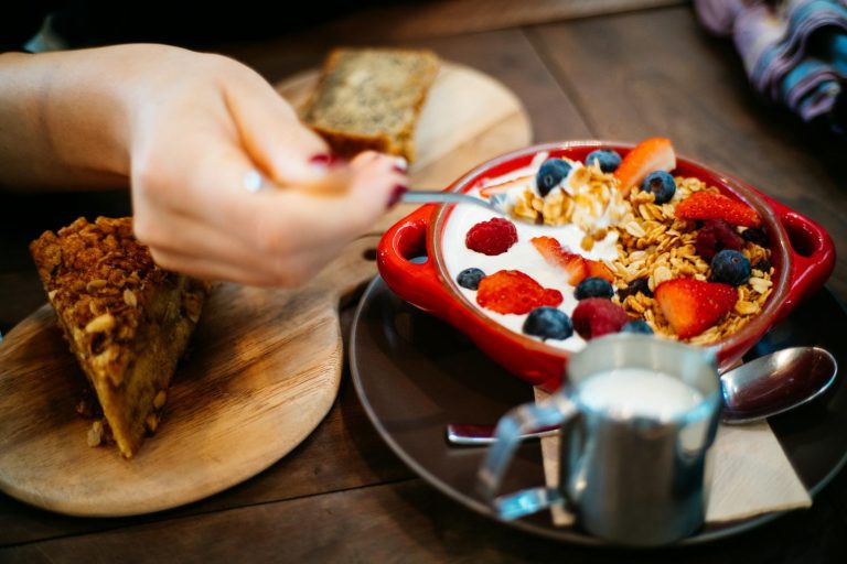 Close-up of a breakfast setting with granola, fresh berries, and a slice of cake.