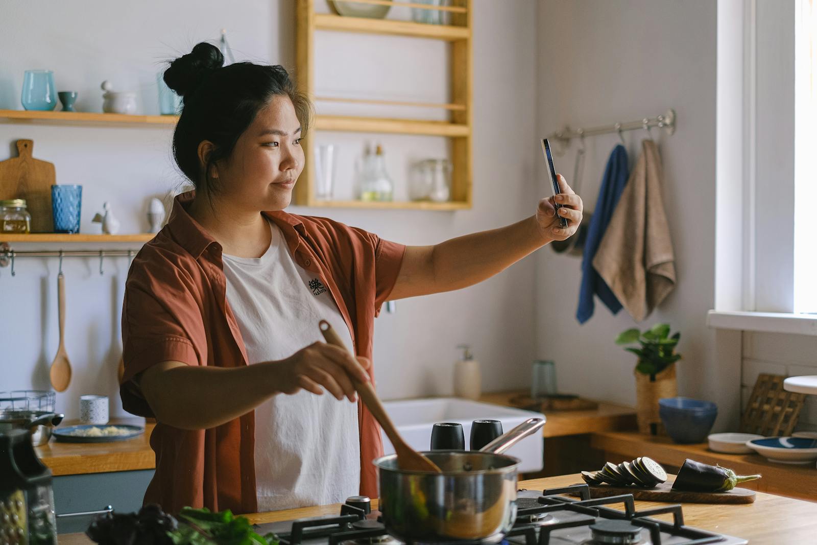 Woman cooking in kitchen and taking selfie, capturing the moment.