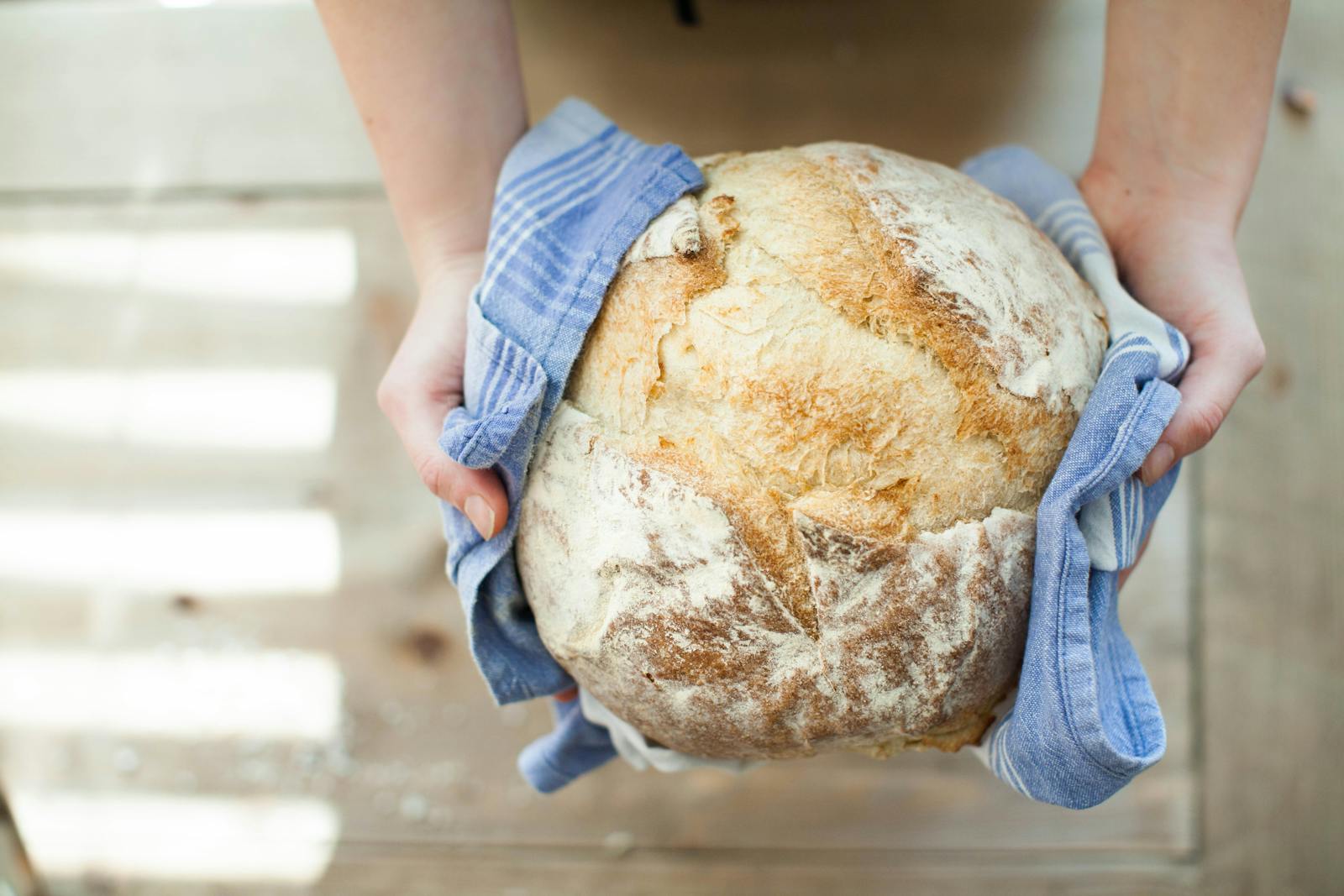 Close-up of artisan bread held in hands with a blue cloth on a wooden table.