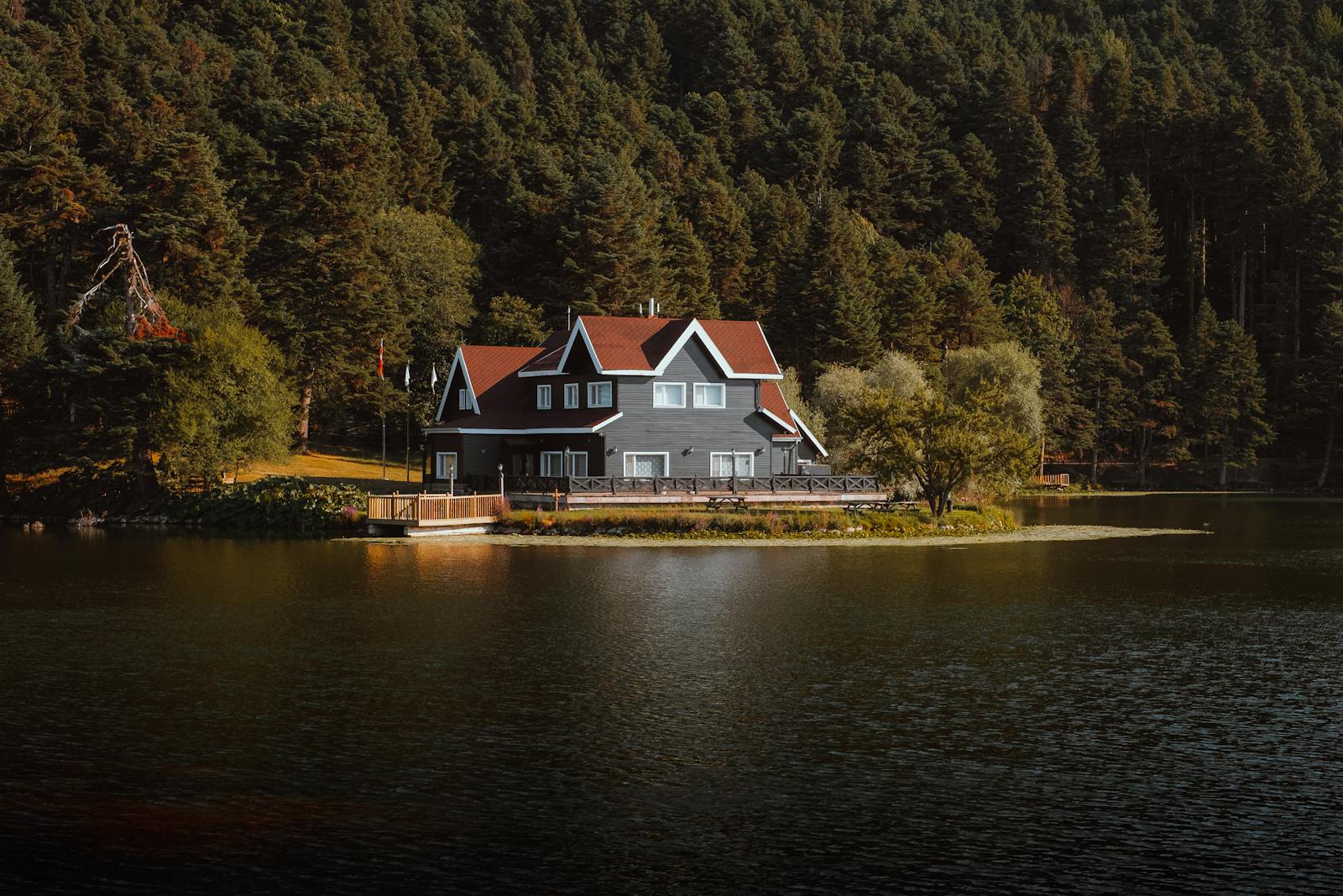 Charming house by a tranquil lake surrounded by dense forest at daytime.